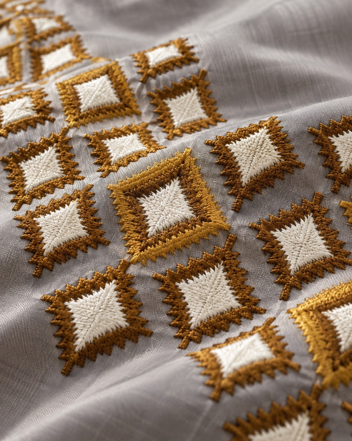 Close-up of mustard and ivory diamond embroidery on grey satin bedsheet